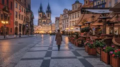 Staroměstské náměstí v Praze při západu slunce, člověk kráčí po dlažbě, historické budovy.