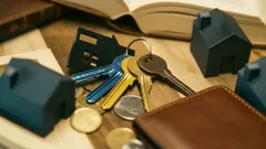 Klíče od domu, modely domků, mince a peněženka – symboly bydlení a financí.