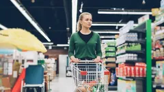 Žena s nákupním košíkem nakupuje v supermarketu mezi regály s potravinami.