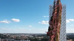 Moderní výšková budova s nápadnou fasádou, modré nebe, městská krajina v pozadí